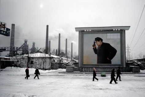 Hiroji Kubota, At the Kim Chaek Ironworks; the billboard shows Kim Il-sung peering into a furnace, Chongjin, North Korea, 1986, dye-transfer print, 20 x 24 inches/50.8 x 61 cm © Hiroji Kubota/Magnum Photos
